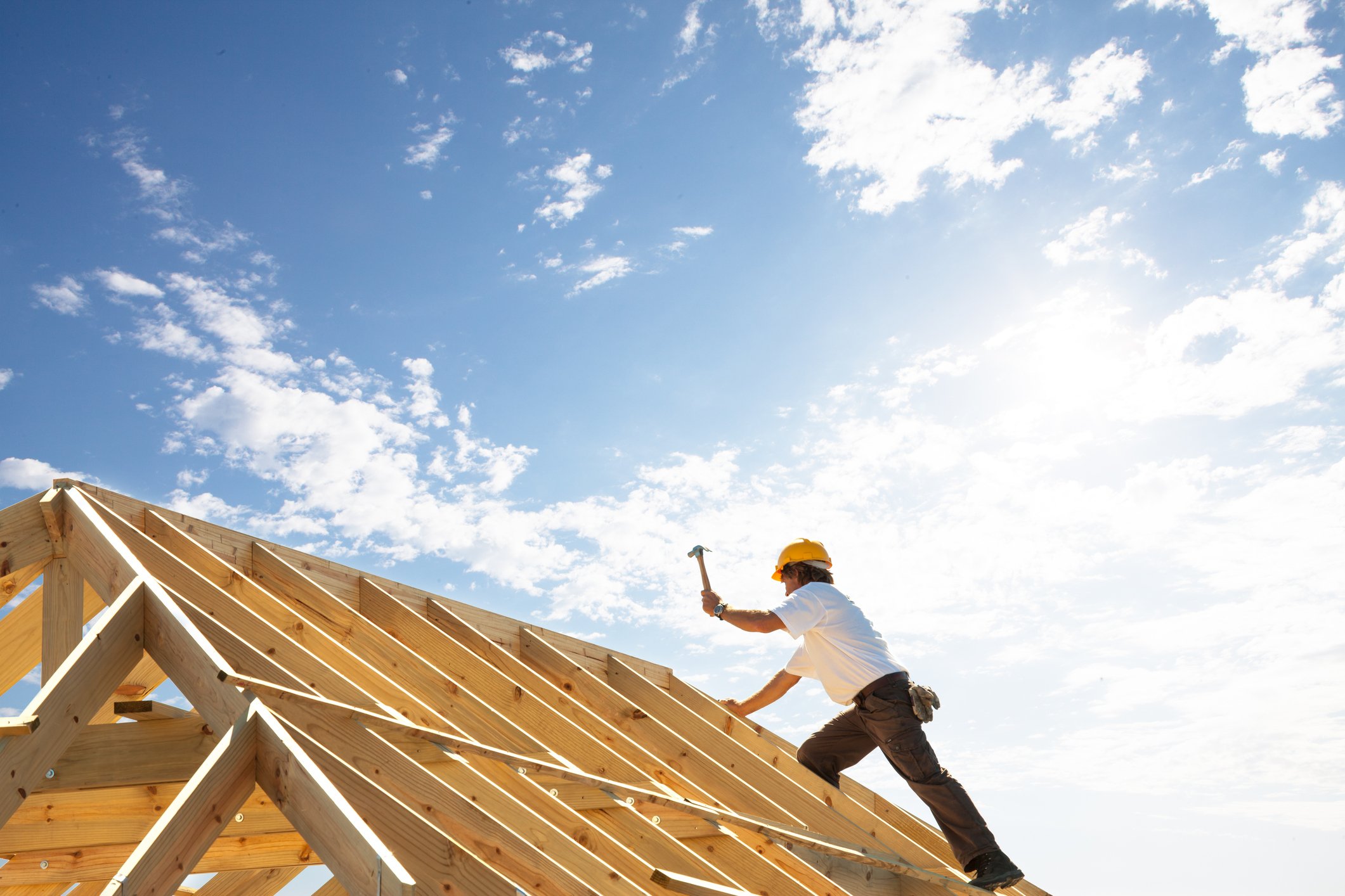 Worker in hard hat swinging a hammer on top of roof beams