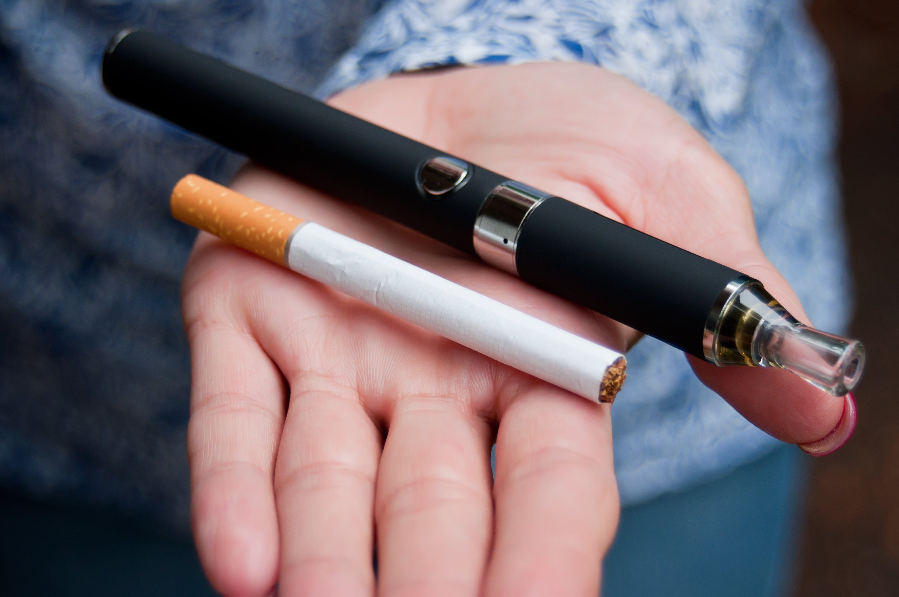 An e-cigarette and a regular cigarette on an outstretched palm.