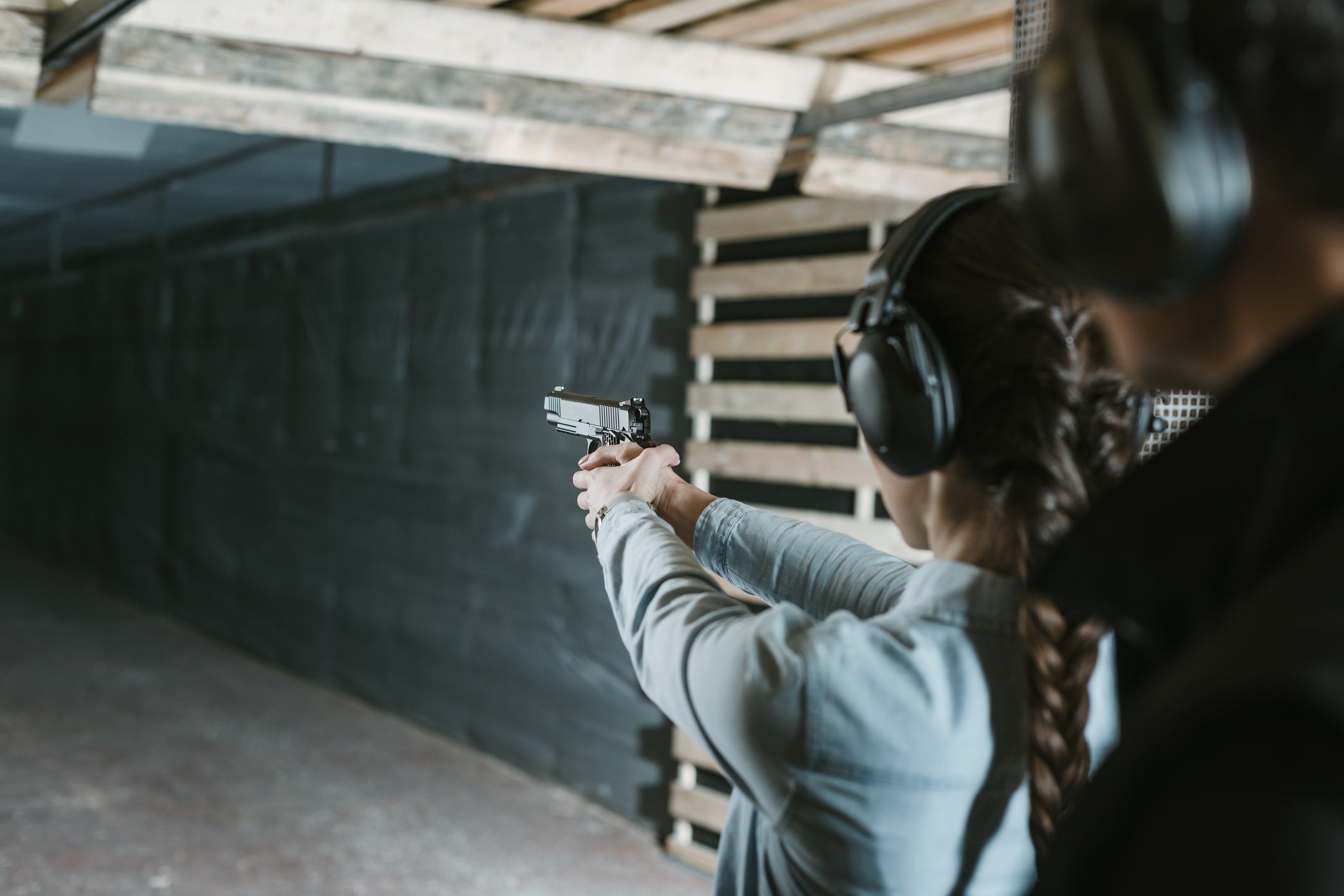 Woman holding handgun at shooting range with instructor behind her