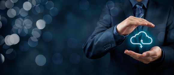 A man in a blue suit with his hands cupping an outline of a blue neon cloud.