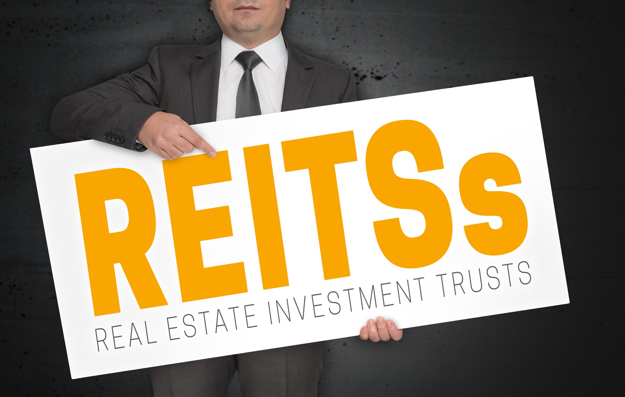 A person in a suit holding a sign that says REITs.