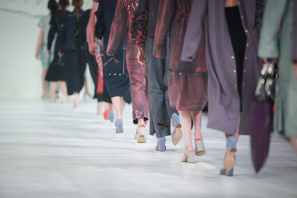 The lower bodies of a parade of fashion models on a runway.
