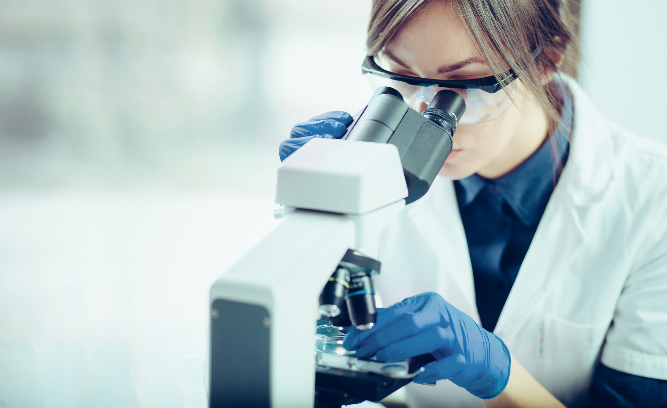 Female scientist in lab coat looking through microscope