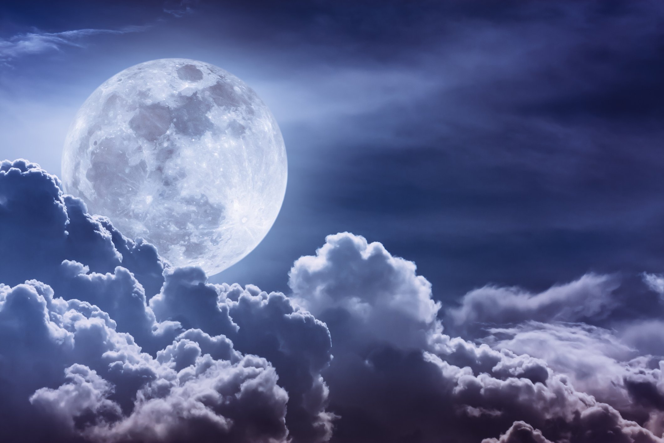 Moon in night sky with white fluffy clouds beneath it