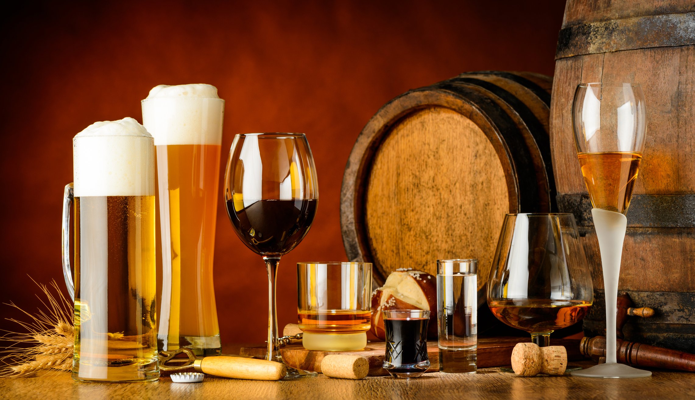 Alcoholic drinks on wooden table in glasses, mugs and shots with barrel in background