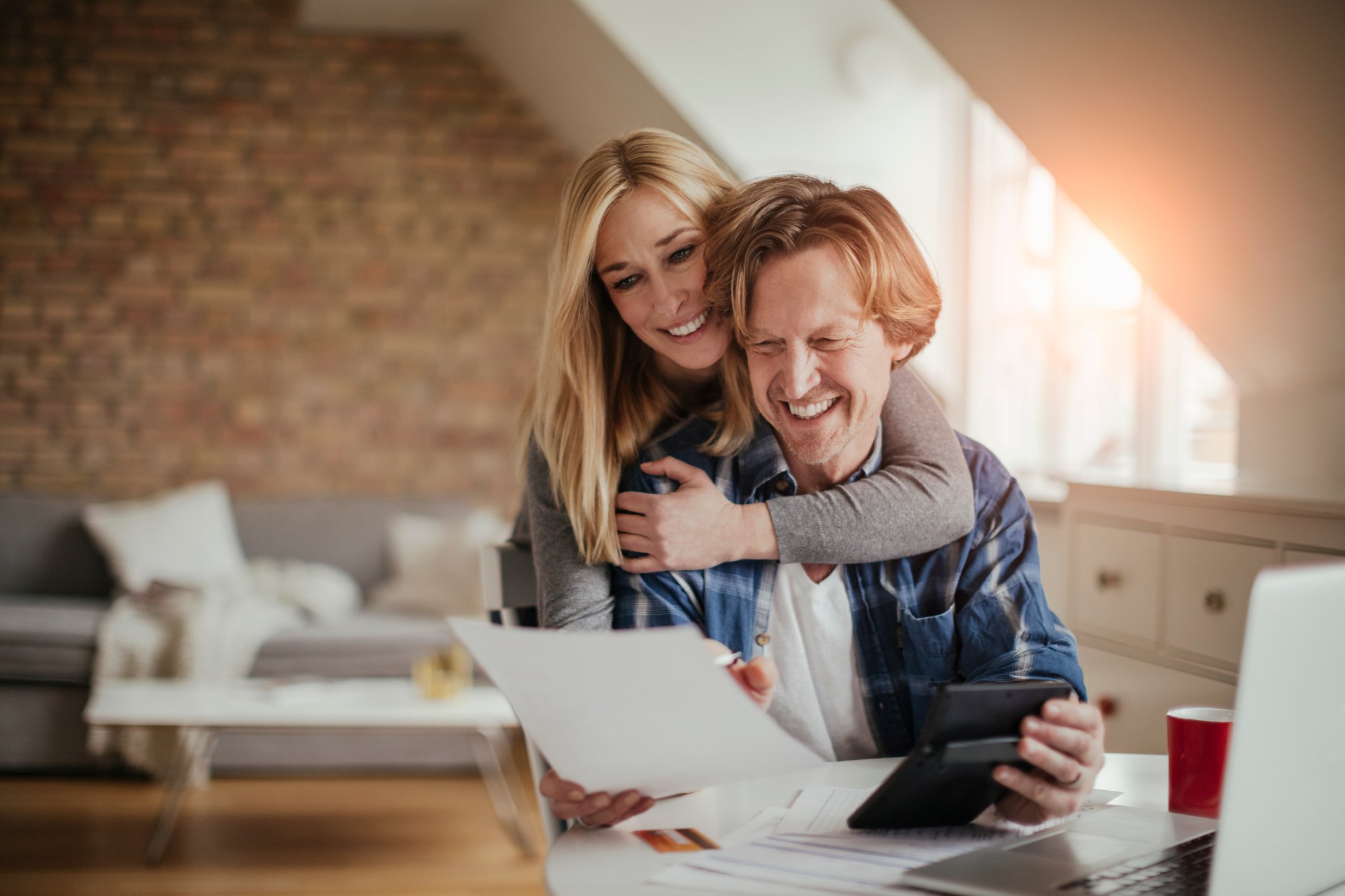 Woman putting arms around man while looking at papers