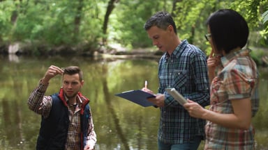 Three people outside examining river water