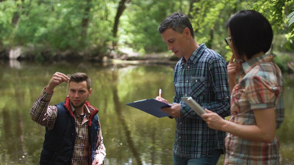 Three people outside examining the water from a river.