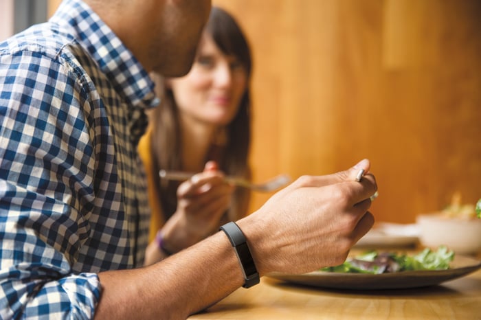 A man eating a healthy meal, with a focus on the Fitbit activity tracker on his wrist. 