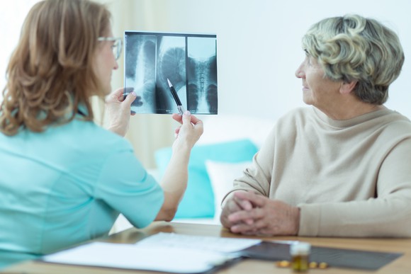 Medical practitioner reviews X-rays with elderly patient.