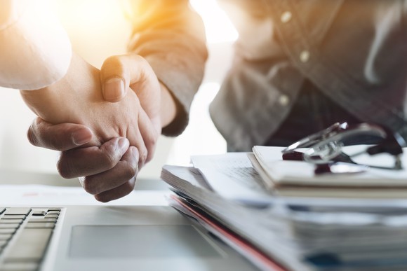 Two businesspeople shake hands over a stack of documents.
