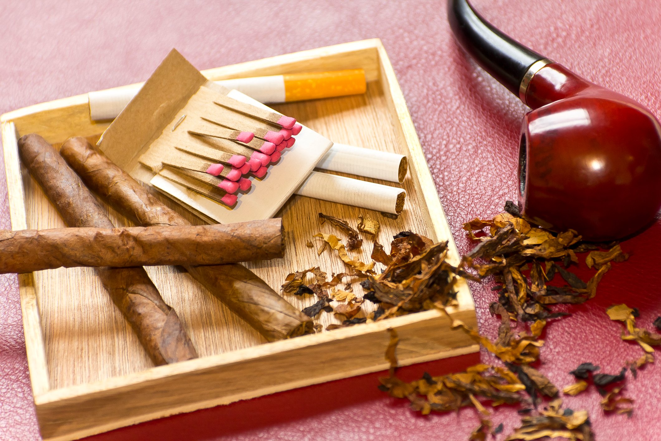 Loose cigarettes and a pack of matches next to a pipe on its side and some loose tobacco