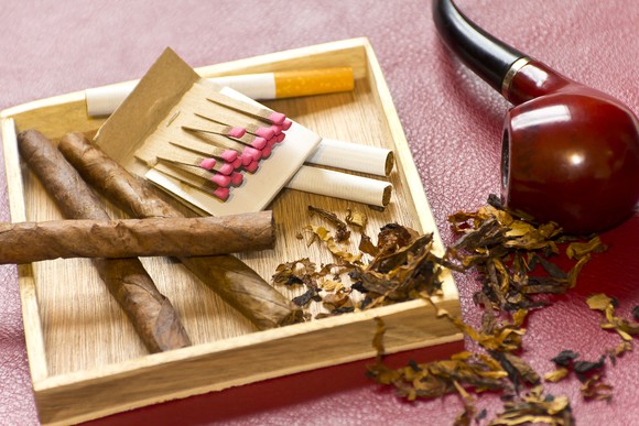 Loose cigarettes and a pack of matches next to a pipe on its side and some loose tobacco