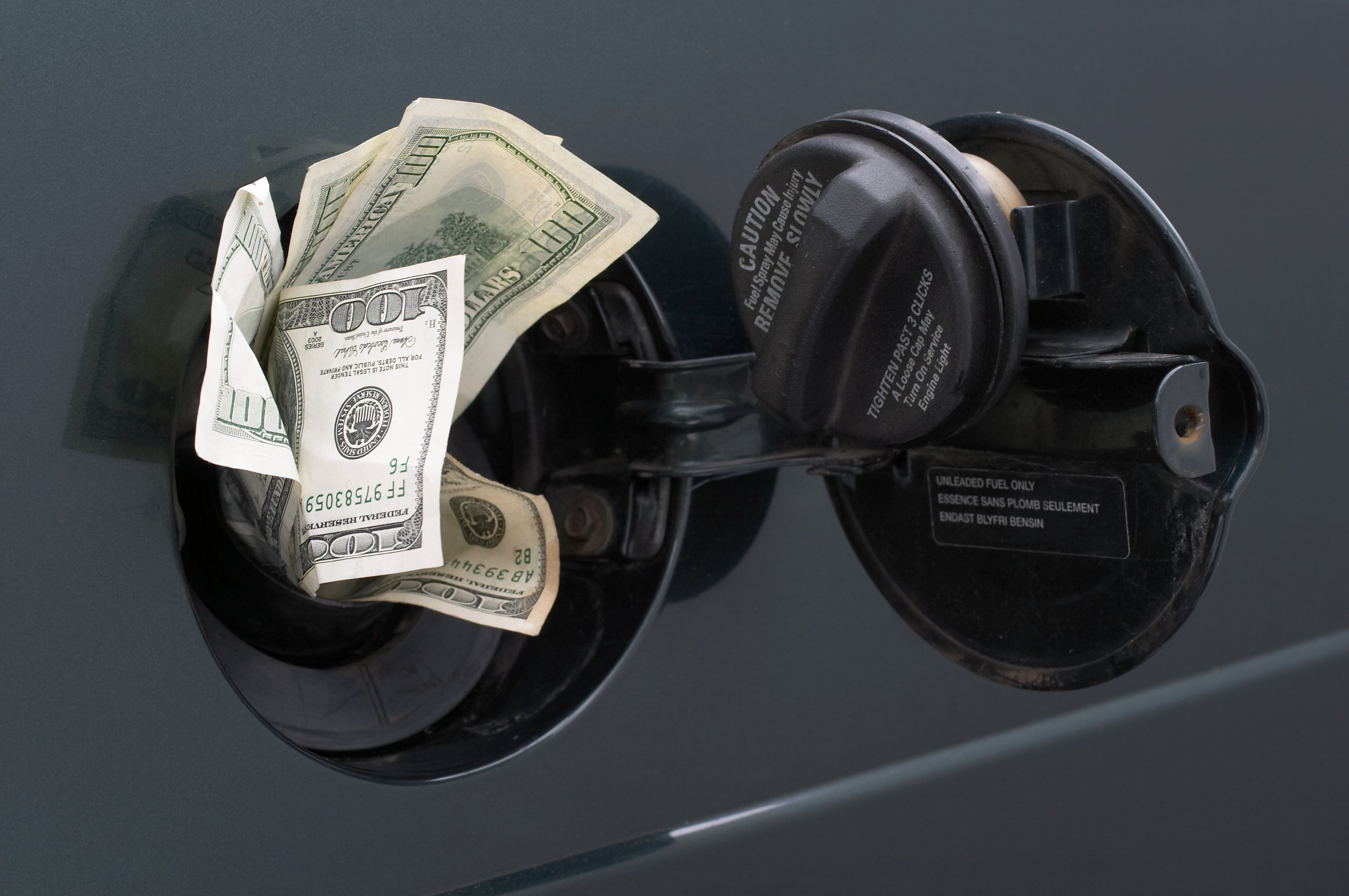 Dollars sticking out of a car gasoline tank.