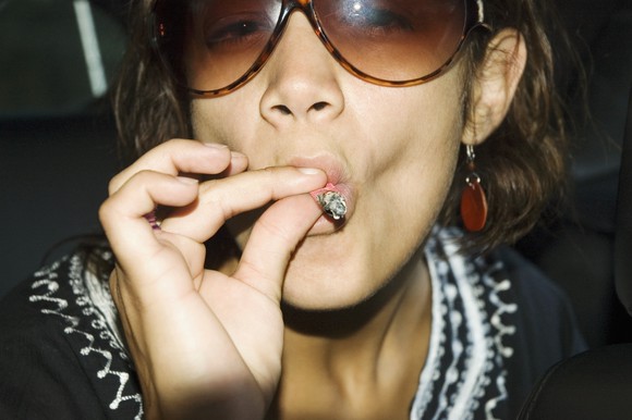 A young woman inhales deeply from a marijuana cigarette.