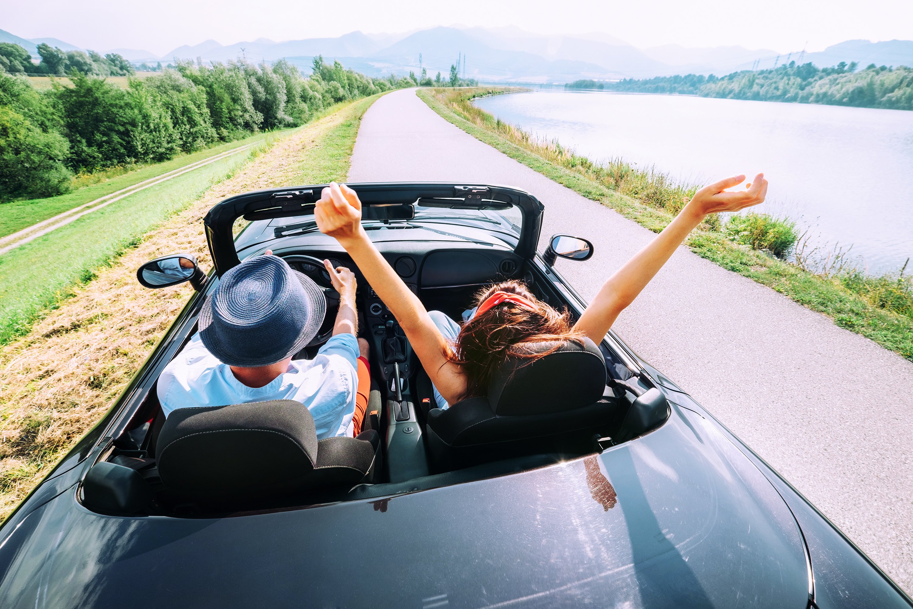 A couple in a convertible drive past a lake