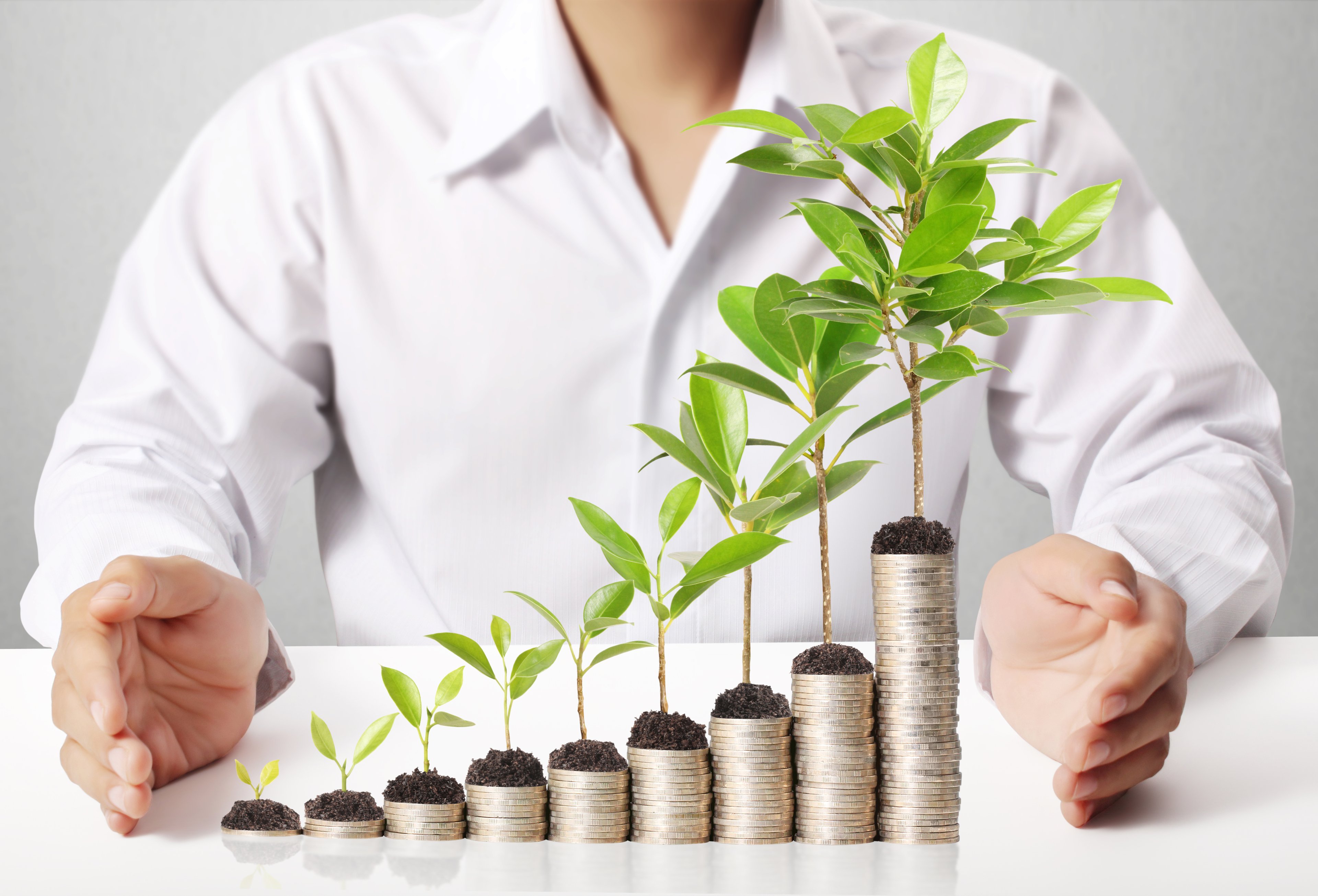 Man with progressively higher stacks of coins in front of him, with green sprouts growing out of them.