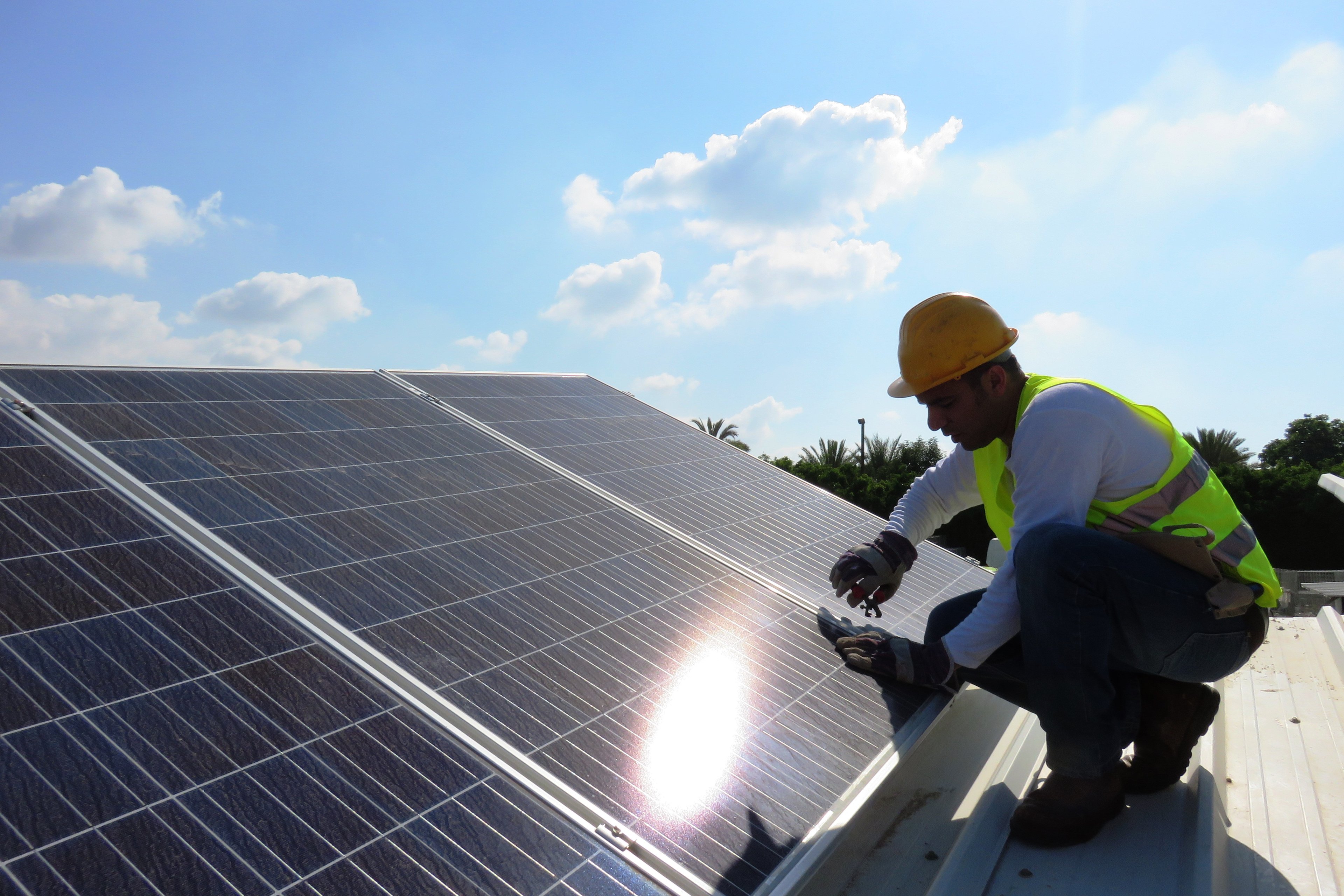 A male worker installs solar panels on a rooftop in sunshine.