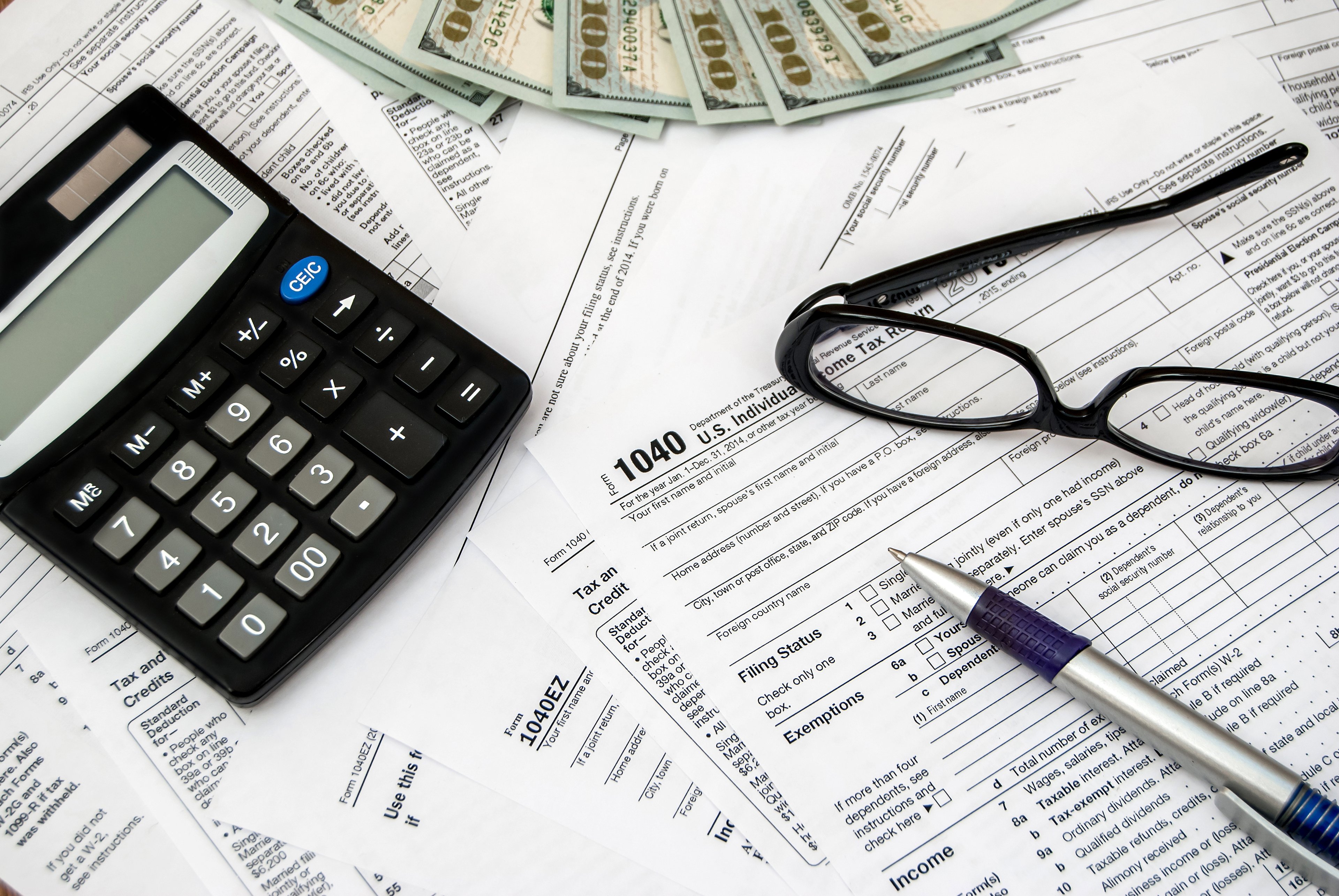 Tax forms with a pen, calculator, cash, and eyeglasses.