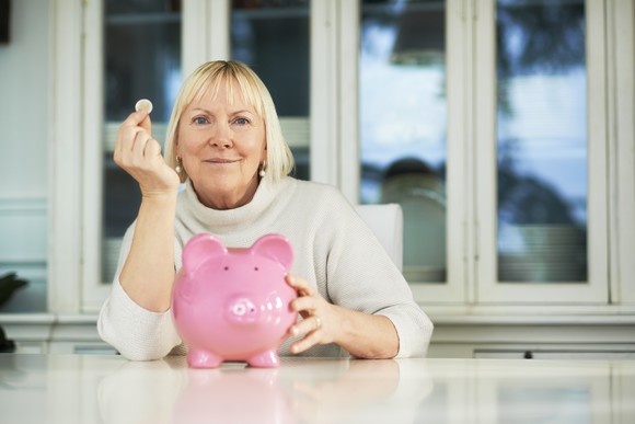 Older woman with a coin and a piggy bank.