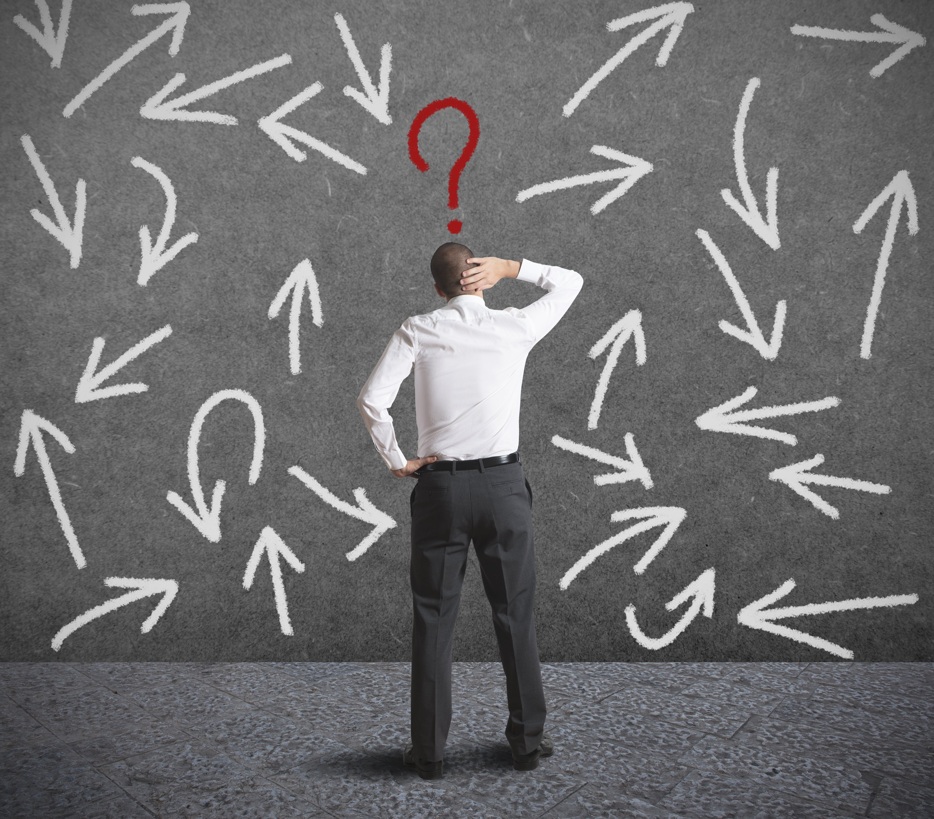 Man scratching head in front of question marks on wall.