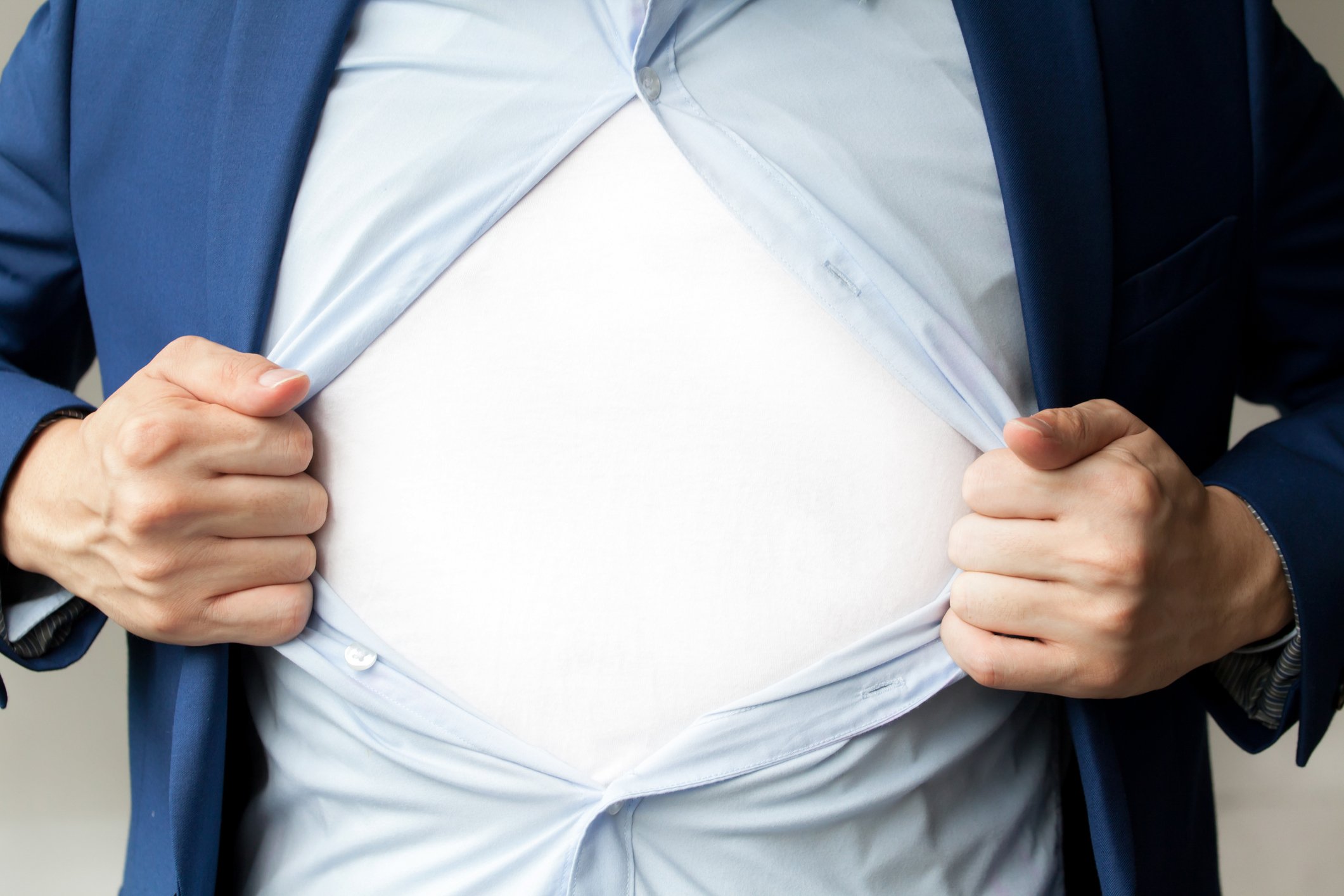 A man opening his button-down shirt to show the white undershirt underneath.