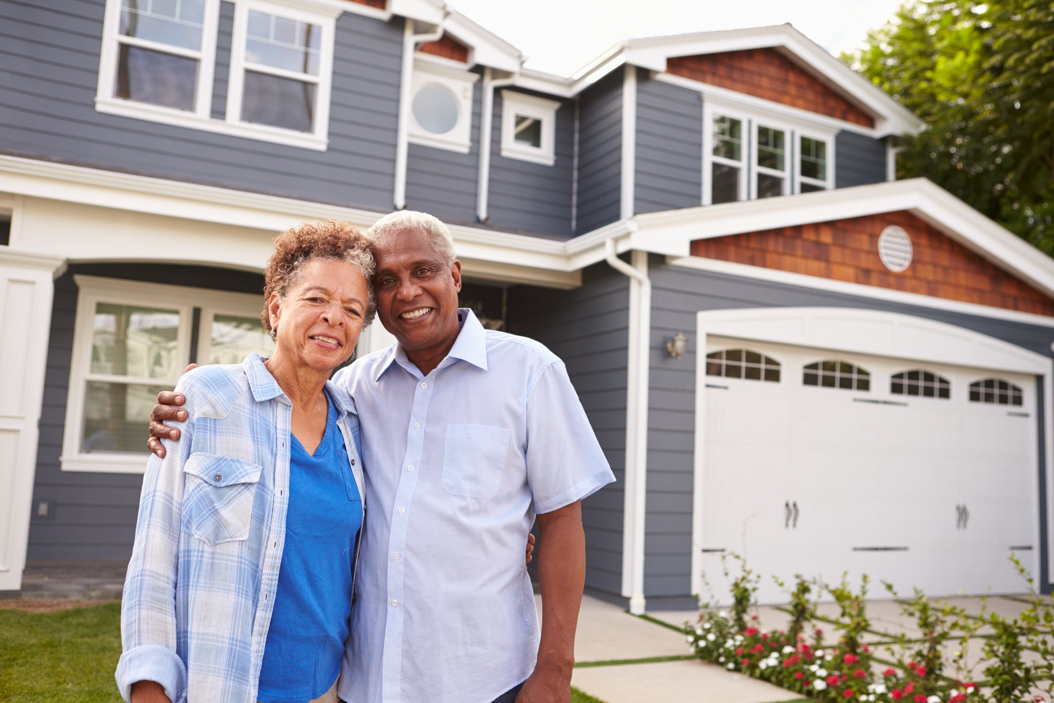 Elderly couple standing outside of their house.