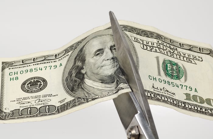 Scissors cutting through a hundred dollar bill. 