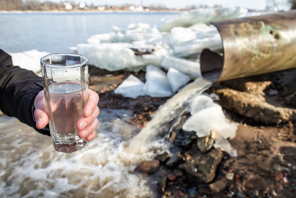 A person holding a drinking glass next to a water treatment facility.