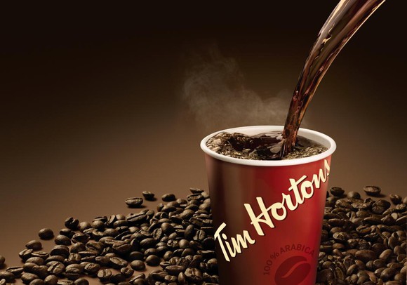 A cup of Tim Horton's coffee being poured surrounded by coffee beans.