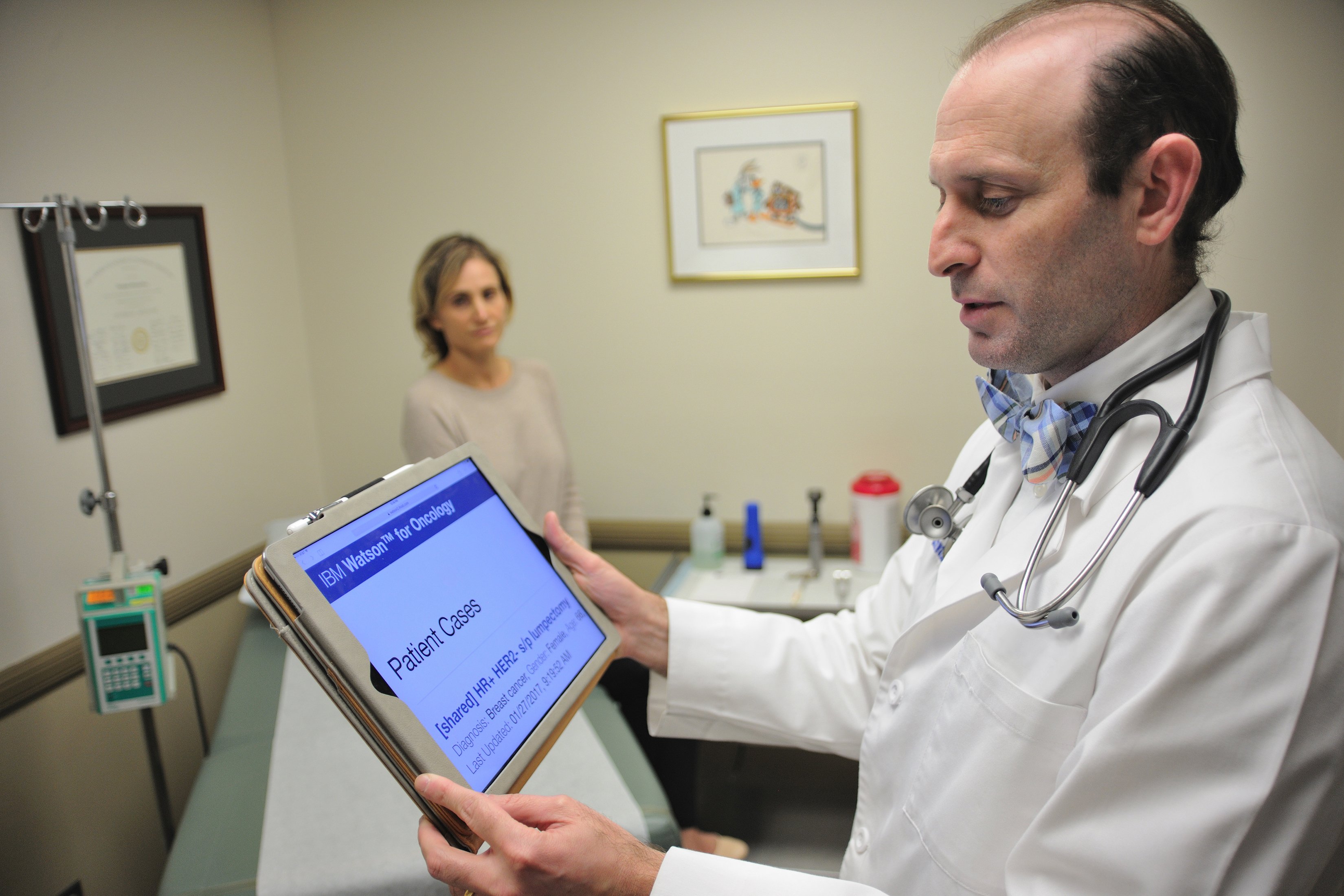Doctor conferring with Watson AI interface on a tablet computer. 