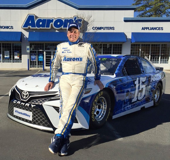 NASCAR driver Michael Waltrip standing in front of his Aaron's-sponsored car and an Aaron's store. 