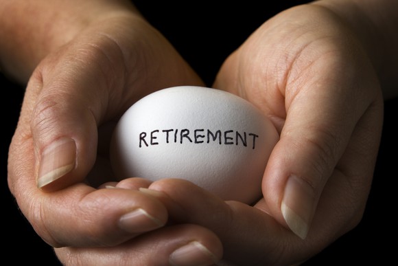 Two hands cradling an egg with the word "retirement" written on it, representing a nest egg.