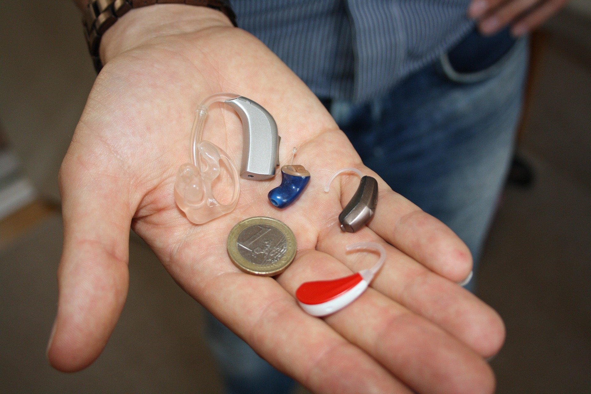 A hearing aid next to a coin in someone's hand to show its relative size.