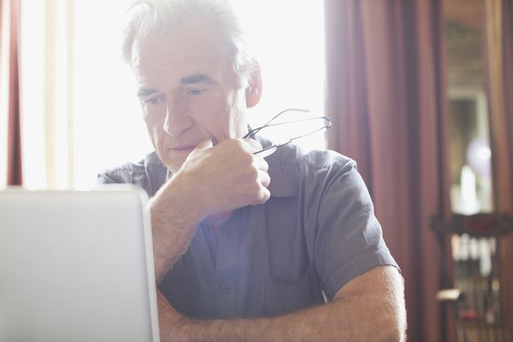 An older man looks pensively at a computer monitor while considering his options.