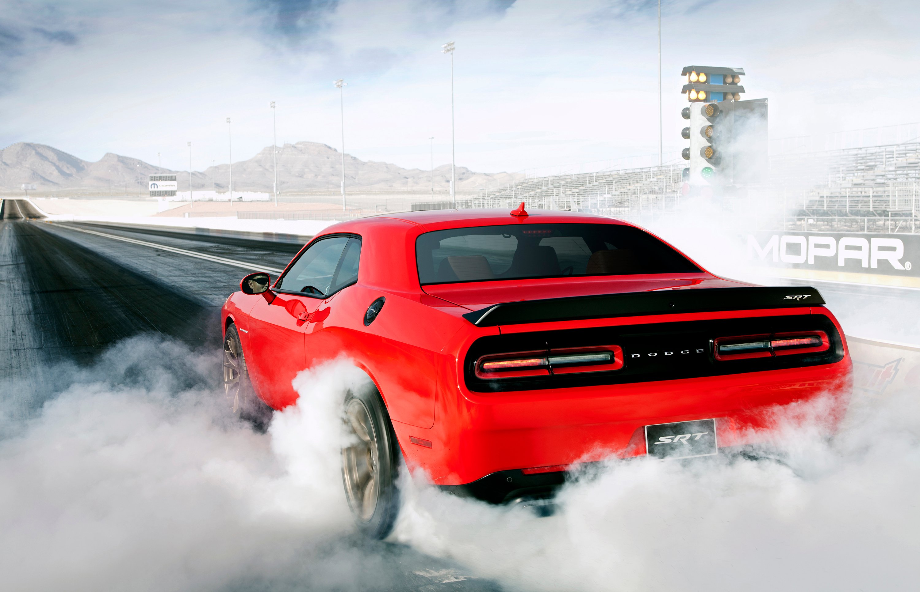 A red Dodge Challenger SRT Hellcat burning rubber on a drag strip. 