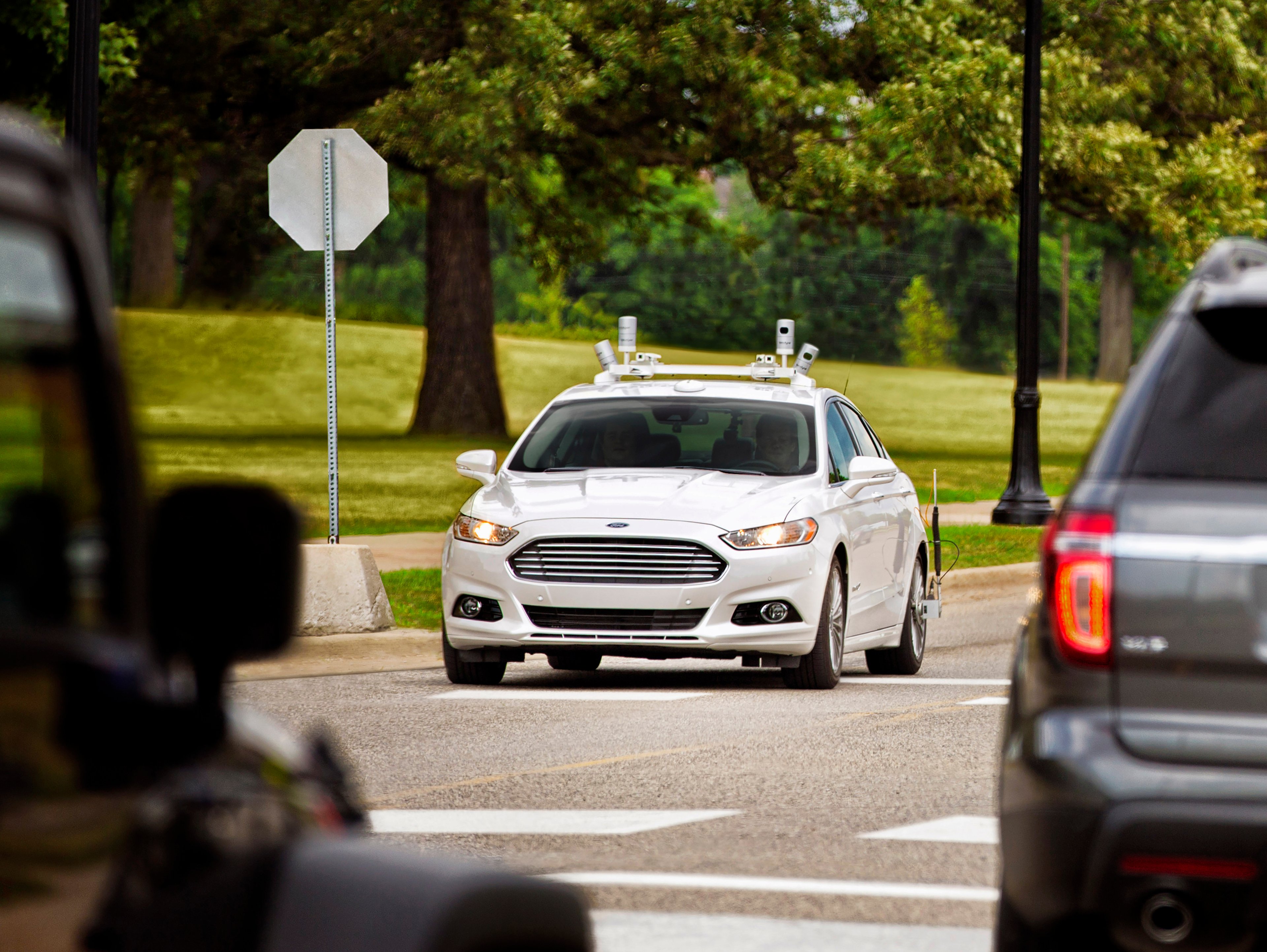 A white Ford Fusion with self-driving sensors on a public road.