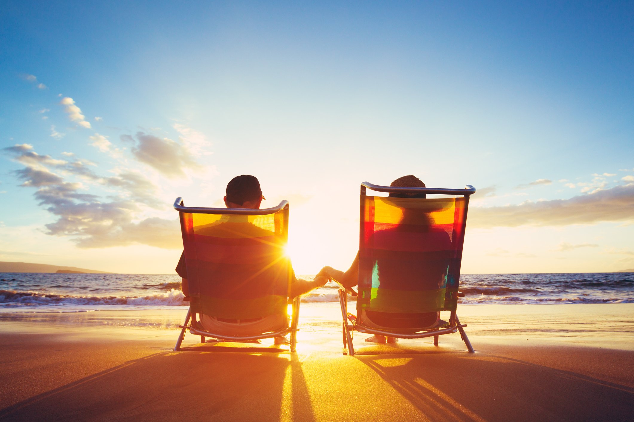 A retired couple watching a sunset on the beach.