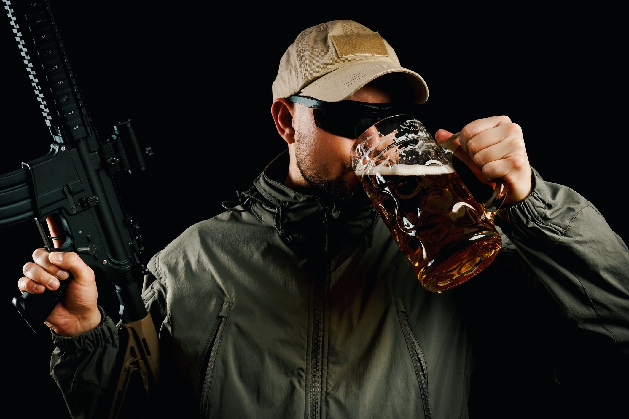 Man drinking from large mug of beer while holding a modern sporting rifle