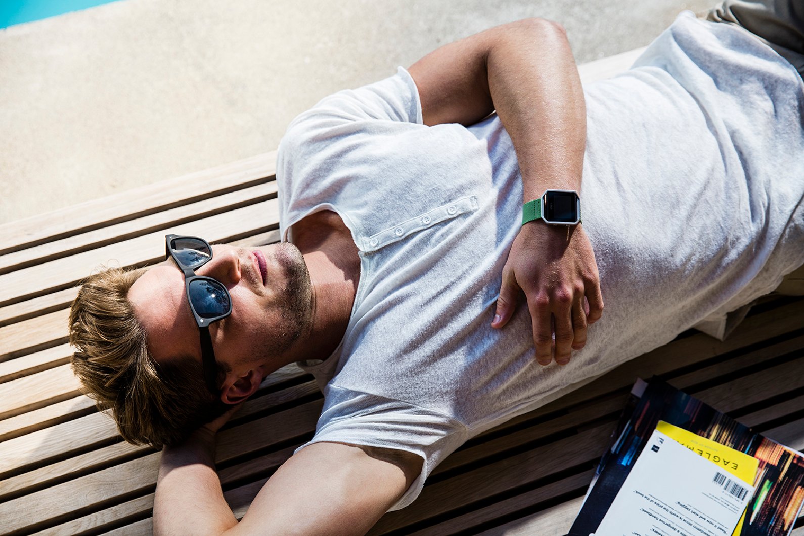 Fit bearded man with sunglasses relaxing with Fitbit Blaze on his wrist.