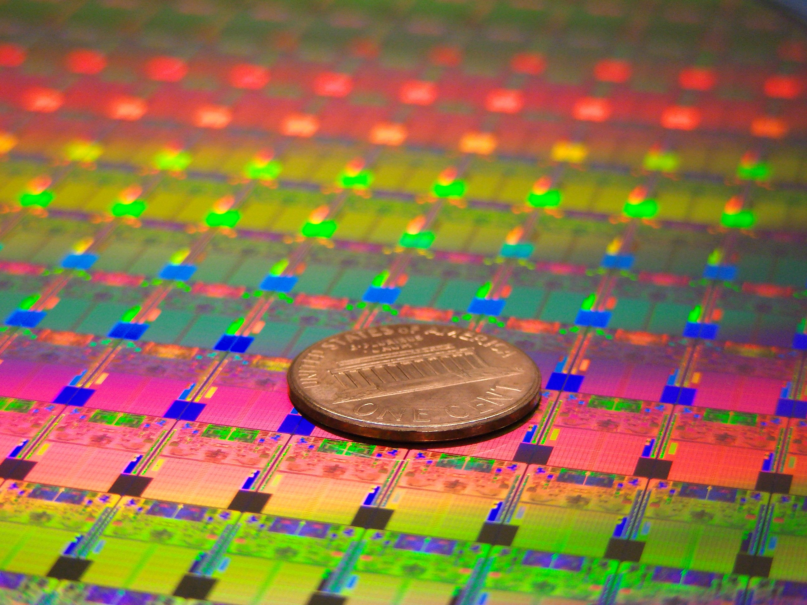 A wafer of chips with a penny on top of it for scale. 