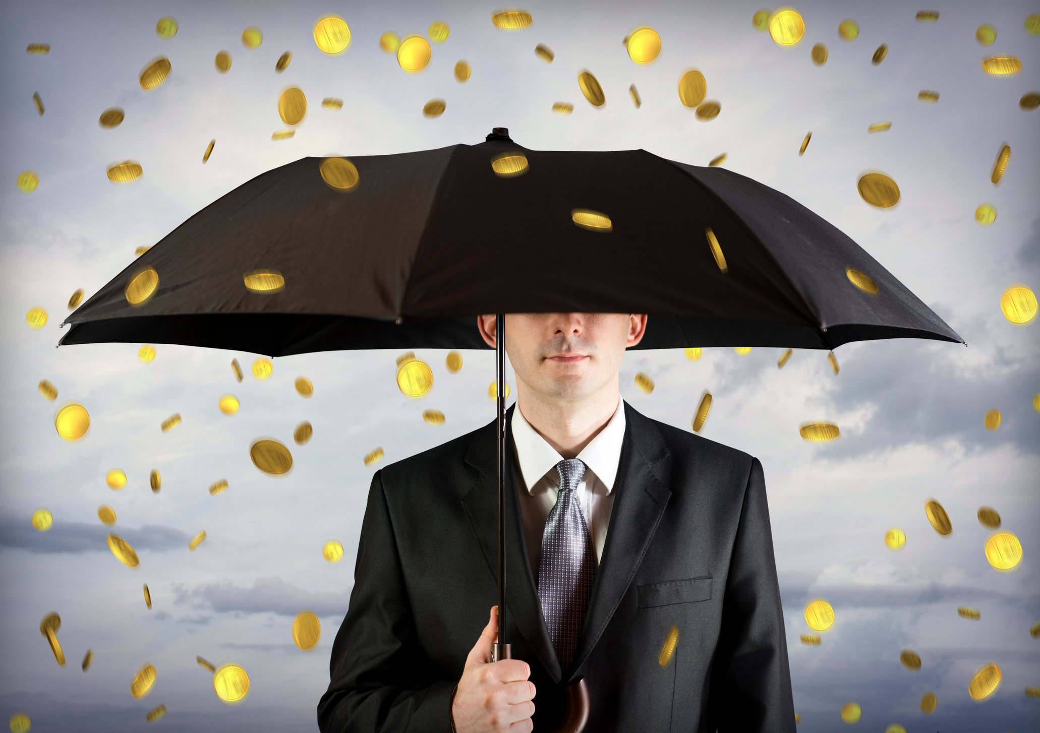 Man in suit holding an umbrella as gold coins fall out of the sky.
