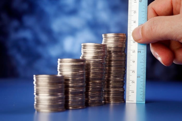 A hand holds a ruler up to stacks of coins