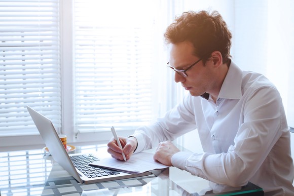 Man reading paper and using laptop.