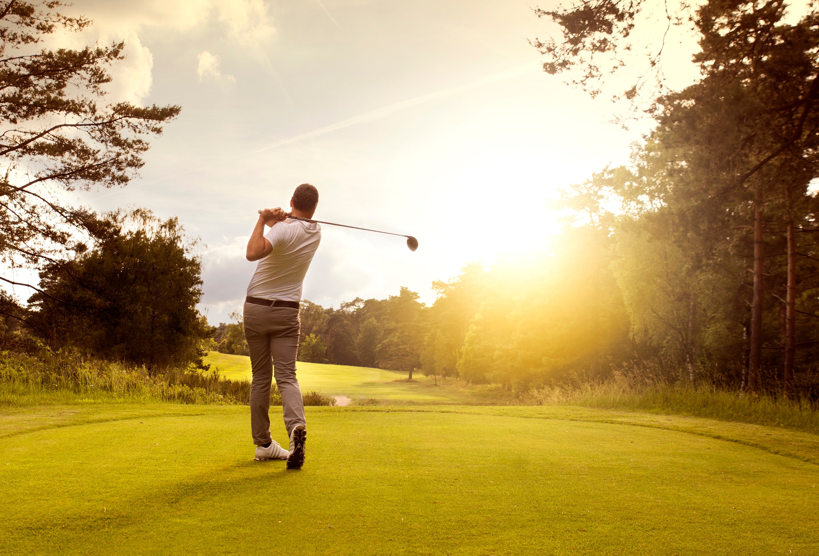 Man teeing off on golf course at sunrise. 