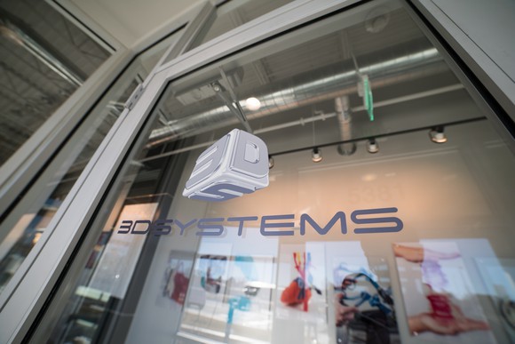 The glass door or window of a 3D Systems' building showing the company's name and logo.