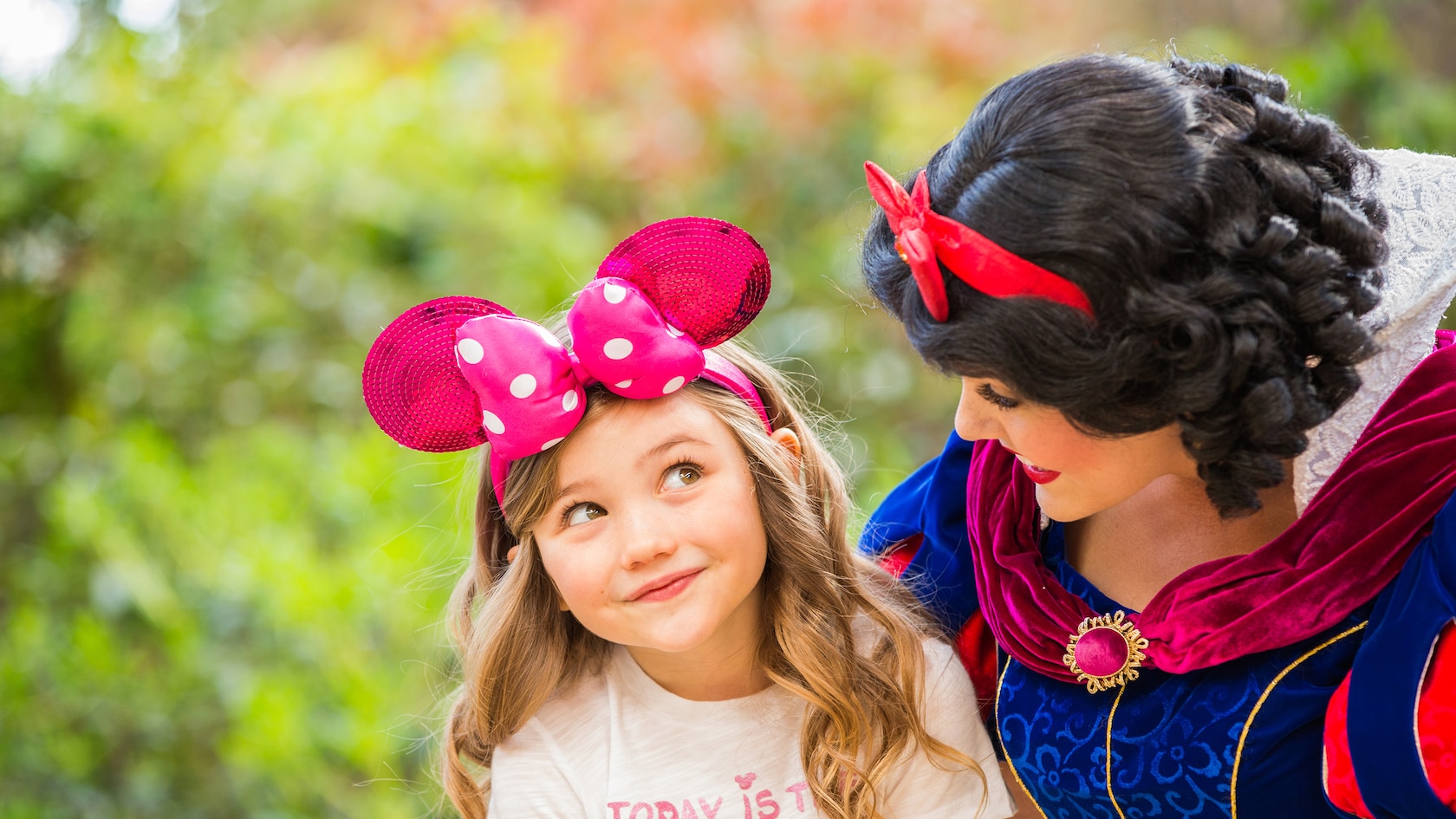A Snow White character interacts with a little girl at a Disney park. 
