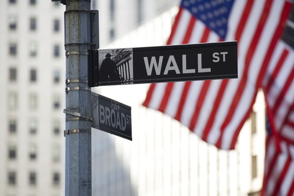 Picture of Wall Street sign with American flag in background.