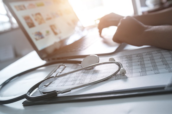 A doctor working on the computer with a stethoscope in the foreground.
