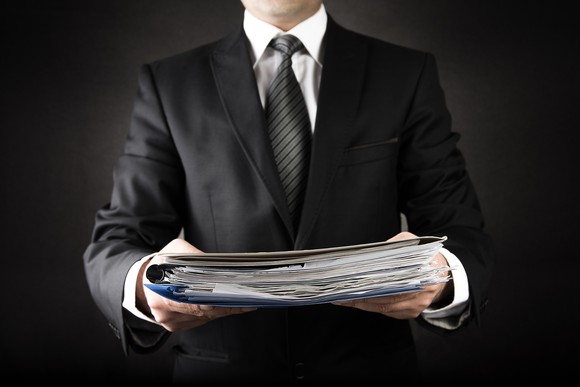 Man wearing a suit holding a pile of documents